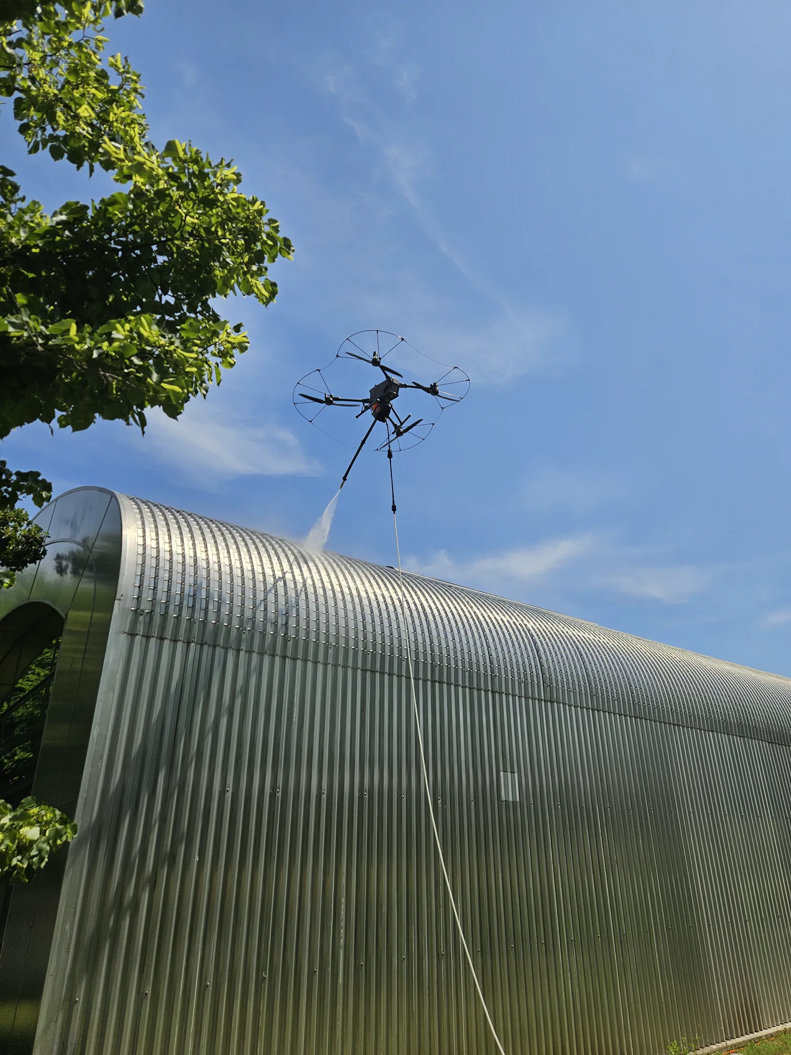 Drone with a cleaning attachment washing a metal building facade