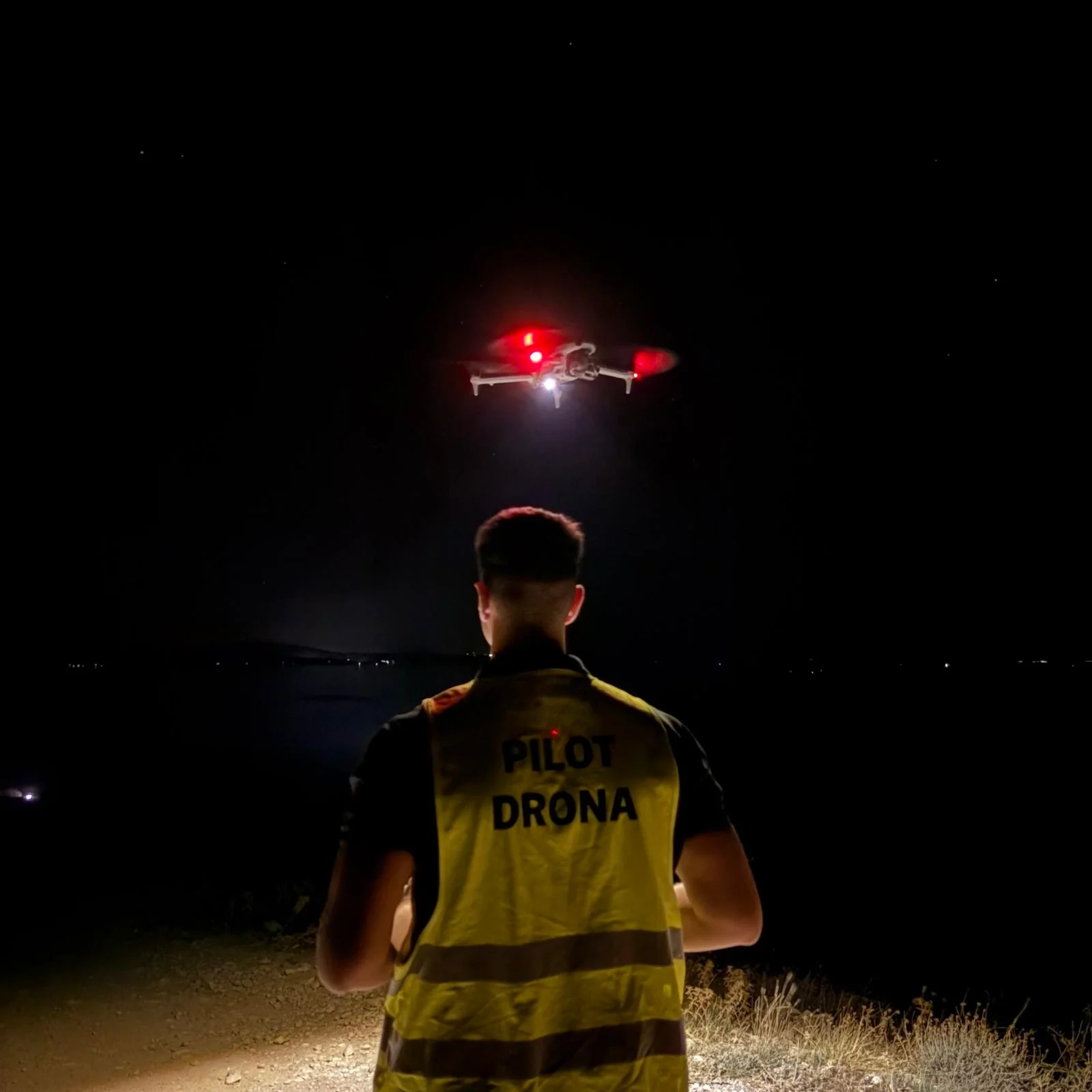 Drone pilot in a high-visibility vest flying a drone at night