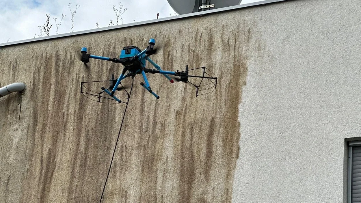 Drone with a cleaning attachment washing a soiled rendered facade